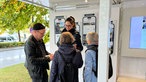 Ein WDR-Stand, an dem sich Menschen aus Warburg mit einer WDR-Reporterin unterhalten.