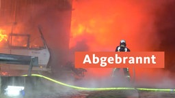 Eine Feuerwehrkraft steht vor den meterhohen Flammen in einer Lagerhalle in Bochum