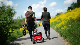 junges Paar geht mit einem Kind im Bollerwagen die Rheinuferpromenade in Leverkusen entlang