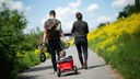 junges Paar geht mit einem Kind im Bollerwagen die Rheinuferpromenade in Leverkusen entlang