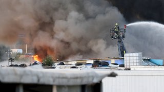Feuerwehrkräfte bekämpfen von einer Drehleiter einen Brand auf einem Schrottplatz