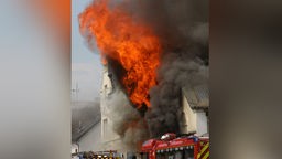 Flammen schlagen aus einem Dach. Ein Motorradladen ist in Sankt Augustin im Rhein-Sieg-Kreis in Brand geraten