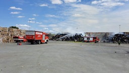 Feuerwehrautos und Einsatzkräfte vor einem Brand, die Einsatzkräfte versuchen den Brand zu löschen.