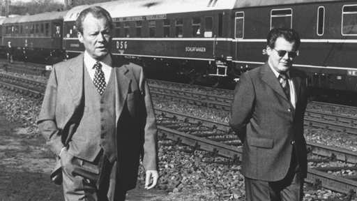Schwarz-Weiß-Foto von Willy Brandt, der neben seinem Referenten Günther Guillaume vor einem Zug entlang läuft