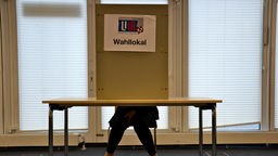 Ein Mädchen sitzt in einer Wahlkabine und gibt ihre Stimme ab