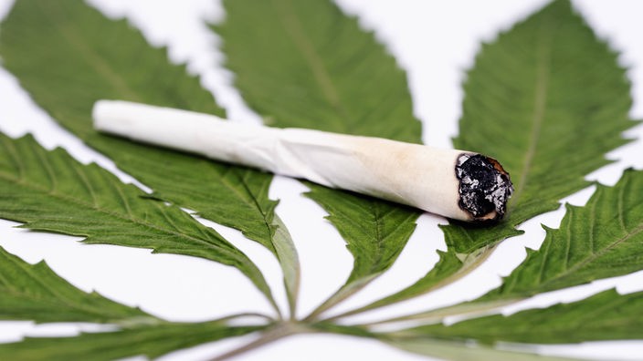 Ein Joint liegt auf einem Cannabisblatt.