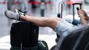 Ein Mann sitzt in der Abflughalle des Flughafens und hat seine Beine auf seinem Koffer abgelegt
