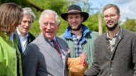 Charles, damaliger Prinz von Wales (3.v.l.), hält bei dem Besuch des Bio-Bauernhofs Herrmannsdorfer Landwerkstätten einen Bruderhahn in den Händen.