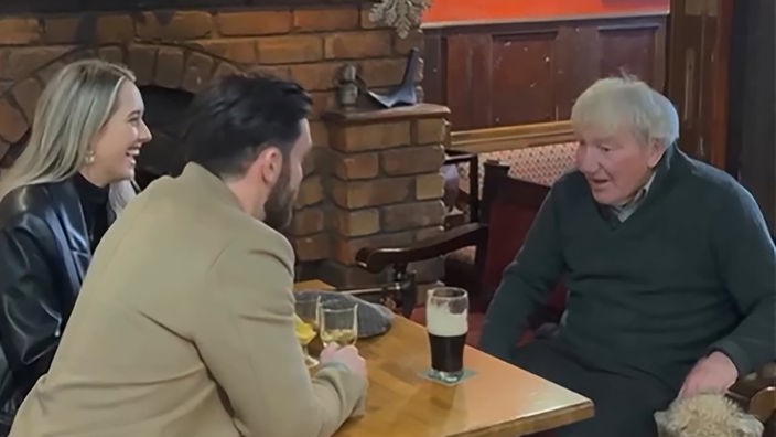 Ein junges Paar sitzt mit einem älteren Mann in einem Pub, trinkt Bier und unterhält sich