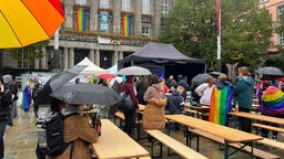 Teilnehmerinnen stehen trotz Regen beim CSD in Wuppertal mit Regenbogenflaggen