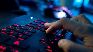 Ein Mann sitzt am Rechner und tippt auf einer rot beleuchteten Tastatur. 