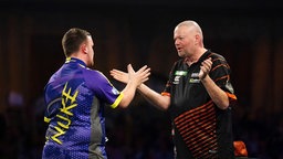 Der Engländer Luke Littler, links, feiert am 30.12.2023 seinen Sieg über den Niederländer Raymond van Barneveld während der Darts-Weltmeisterschaft im Alexandra Palace in London