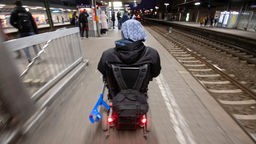 Steffen Gödecke fährt mit seinem Elektro-Rollstuhl am Bahnhof an einem Gleis
