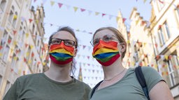 Zwei Teilnehmende tragen einen Mundschutz in den Farben der LGBTQ-Flagge