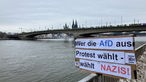 Im Hintergrund die Deutzer Brücke und der Dom, vorne ein Schild mit der Aufschrift "Wer die AfD aus Protest wählt, wählt Nazis"