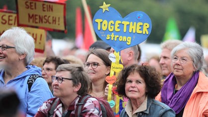 Demonstrierende in Köln halten Schilder hoch mit den Aufschriften "Together we are strong" und "Sei ein Mensch!".