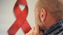 Mit HIV infizierte Person sitzt vor Symbol der deutschen Aidshilfe