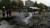Dnipro, Ukraine: Feuerwehrleute und Polizisten arbeiten an der Stelle, an der eine Explosion nach einem russischen Angriff auf der Straße einen Krater hinterlassen hat