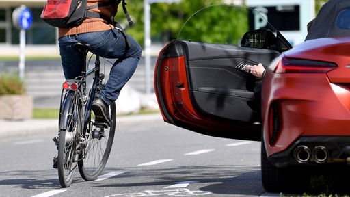 Ein Mensch auf einem Fahrrad, der gerade einer geöffneten Autotür ausweicht.