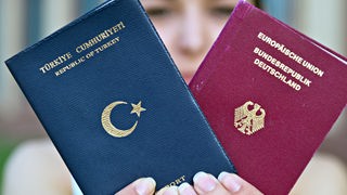 Eine Frau hält einen türkischen Pass und einen deutschen Reisepass in den Händen