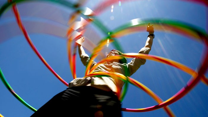 Aufnahme von unten zeigt ein Mädchen mit mehreren bunten Hula-Hoop-Reifen.