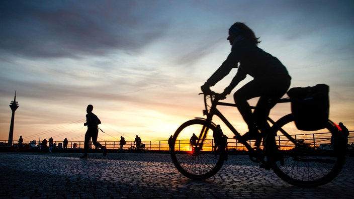 Eine Frau fährt mit einem Fahrrad während des Sonnenuntergangs am Rhein entlang