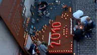 Menschen stellen Kerzen  als Jahreszahl 2010 vor Gedenktafel auf; 