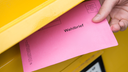 Ein pinker Wahlbrief wird in einen Briefkasten geschmissen