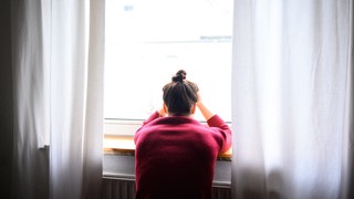 Eine Frau sitzt mit Kopf in den Händen einsam am Fenster