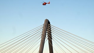 Ein Hubschrauber fliegt über die Brücke, um durch den Wind das Eis herunter zu wehen