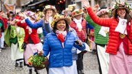 Frauen in bunten Jacken und mit Blumen geschmückten Hüten feiern und tanzen bei der Düsseldorfer Karnevals-Sessionseröffnung