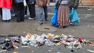 Müll auf der zülpicher Straße, dahinter sind Feiernde zu sehen.