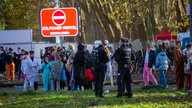 Polizei-Beamte vor einer Menge von Feiernden, im Hintergrund ist eine digitale Anzeige mit "Zülpicher Viertel geschlossen" zu sehen