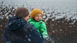 Ein Vater hält sein Kind im Schnee auf dem Arm