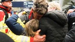 Ein Mann, der im Krisengebiet der Türkei war, umarmt eine Frau und ein Kind. Die Rettungskräfte werden von jubelnden Menschen auf dem Flughafen in Köln begrüßt