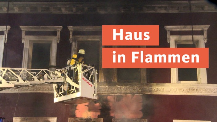Brennendes Haus, zwei Feuerwehrleute auf einem Rettungkorb an einem Kran, daneben die Bannerschrift "Sprung aus Fenster"