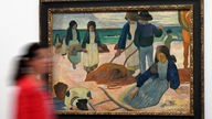 Eine Besucherin geht am Bild ·Bretonische Tangsammlerinnen (II)· aus dem Jahr 1889 von Paul Gauguin vorbei.