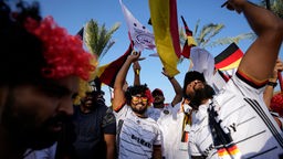 Mehrere Fans mit Artikeln der deutschen Nationalmannschaft und Flaggen jubeln in Katar.