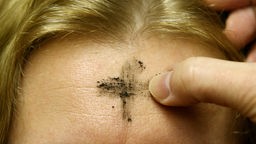 Ein Aschenkreuz bekommt eine Katholikin in der St. Michael-Kirche am Wasserturm in Essen auf die Stirn gemalt.