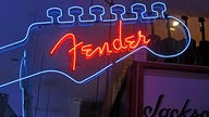 Blaue Neonreklame in Gitarrenhalsform mit roter Schrift "Fender"