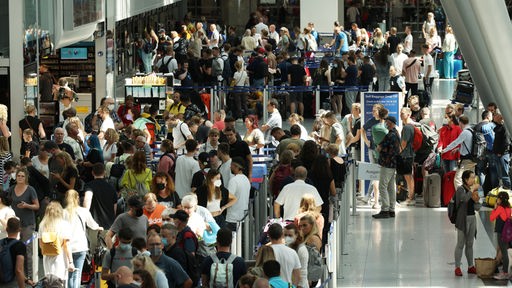 Reisende stehen im Flughafen in langen Warteschlangen an der Gepäckabgabe des Düsseldorfer Flughafens an