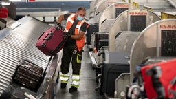 Ein Arbeiter hebt im Gepäckverteiler des Flughafen Stuttgart einen Koffer von einem Gepäckband auf einen Gepäcktransportwagen. 