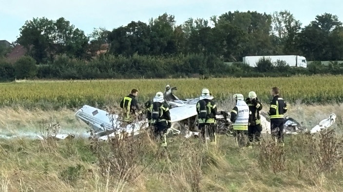 Trümmerteile eines Flugzeugs und Feuerwehrleute auf einem Feld in Bad Sassendorf 