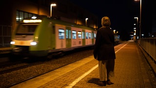 Ältere Frau wartet bei Nacht am Bahnsteig auf ihren Zug