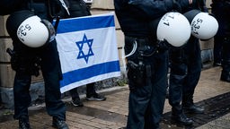  Ein Mann zeigt am Rande einer Propalästinensische Demonstration die israelische Fahne und ist dabei schützend von Polizisten umringt.