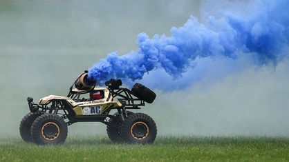 Ferngesteuertes Auto fährt mit blauer Rauchsäule über den Rasen im Fußballstadion