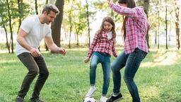 Fröhliches Mädchen spielt Fußball mit ihren Eltern im Park