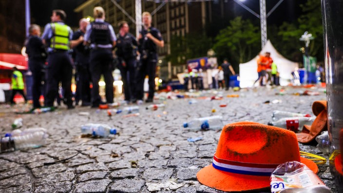 Am Friedensplatz liegt nach der Niederlage der Niederlande gegen England ein orangefarbener Hut auf dem Boden, dahinter Polizeibeamte