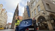 Zwei Männer halten Fahne am Prinzipalmarkt in Münster hoch