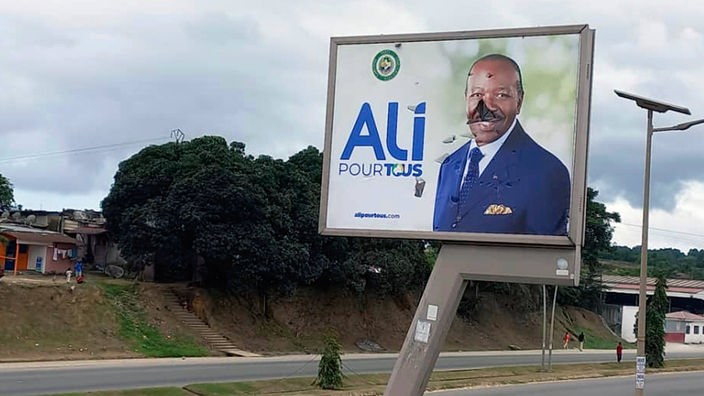 Libreville: Blick auf ein verunstaltetes Plakat des gabunischen Präsidenten Ondimba an einer leeren Straße.